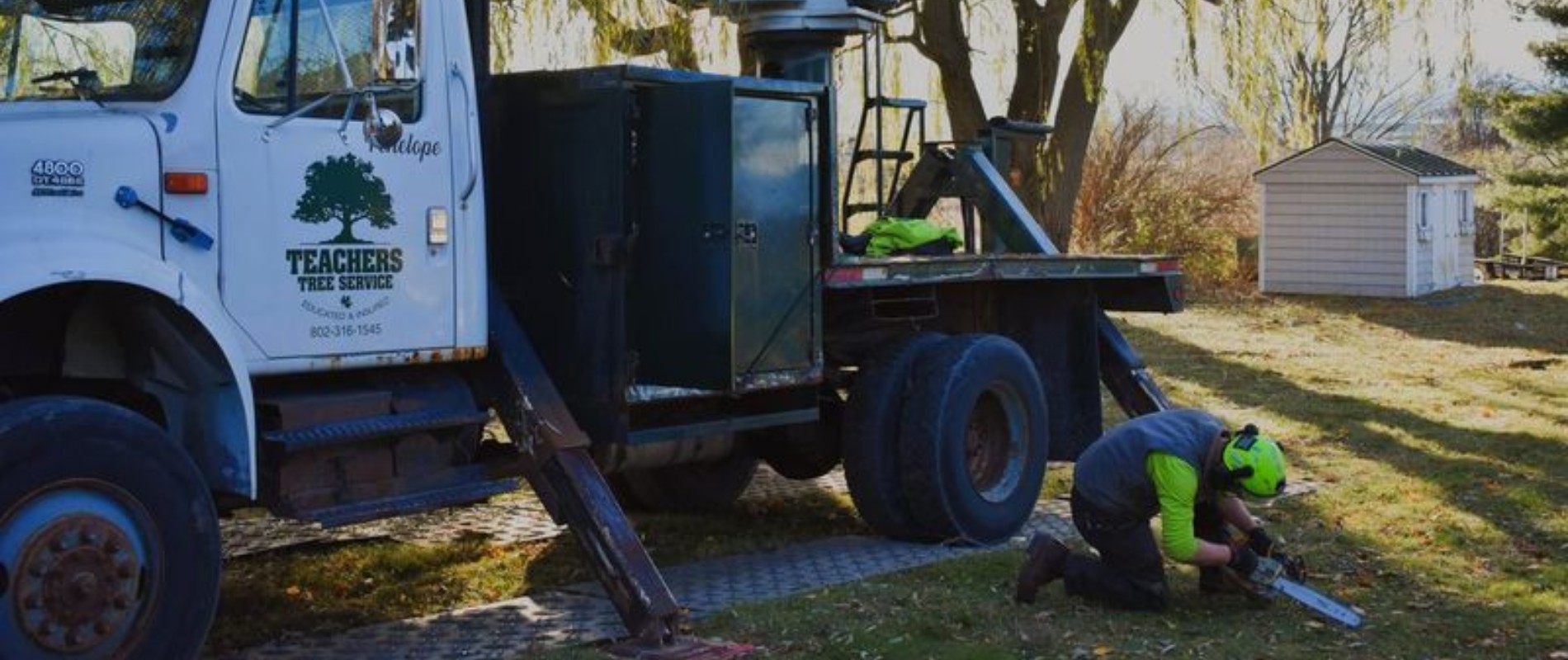 Teachers Tree Service crane truck on a property with an arborist preparing a chainsaw