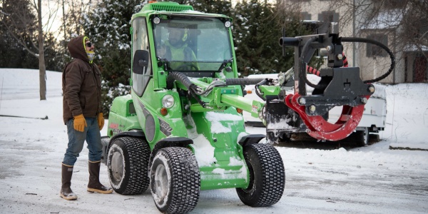 Crew operating compact loader with grapple attachment in snowy conditions during ice storm response