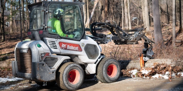 Arborist operating a Bobcat skid steer with grapple attachment during ice storm cleanup