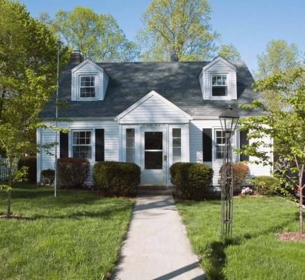 White Cape Cod home with manicured shrubs and trees in the front yard