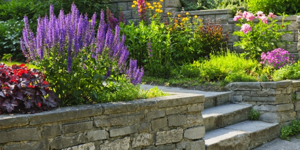 Tiered stone retaining wall with colorful flower beds and stone steps in a landscaped property